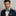 Man wearing a navy suit with a green paisley patterned bow tie and pocket square against a gray background