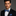 Man wearing a black suit with a blue bow tie and pocket square on a gray background