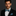 Man wearing a black suit with a white shirt and blue and teal bow tie and pocket square on a dark background