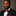 Man wearing a black suit with an orange and black floral and stripe bow tie and pocket square against a gray background