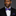 Man wearing a black suit with a white shirt and purple stripe and floral bow tie and pocket square on a gray background