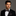 Man wearing a black tuxedo with a patterned dark blue and brown paisley bow tie and pocket square on a gray background
