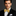 Man wearing a black suit with a gold and brown paisley bow tie with an accenting square against a dark background