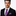 Man wearing a black suit with a purple paisley tie and pocket square on a white background