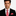 Man wearing a black suit with a red patterned tie and pocket square on a white background
