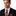Man wearing a dark suit with a orange and brown paisley patterned tie and pocket square on a white background