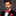Man wearing a black suit with a red plaid bow tie and pocket square on a gray background