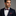 Man wearing a navy suit with a red and blue plaid bow tie and pocket square on a gray background