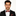Man wearing a black suit with a red and black plaid bow tie and pocket square on a white background