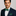Man wearing a navy suit with a green plaid bow tie and pocket square on a gray background