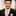 Man wearing a black suit with a pink polka dot tie and pocket square, smiling outdoors.