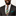 Man wearing dark grey suit with green, orange and yellow plaid necktie and green square