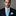 Man wearing a black suit with a blue tie and pocket square against a gray background