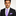 Man wearing a black suit with a purple tie and pocket square on a light gray background