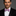 Man wearing a black suit with a white shirt and pink bow tie against a gray background