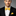 Man wearing a black suit with a yellow and blue polka bow tie and pocket square on a gray background