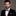 Man wearing a black suit with a grey and pink stripe bow tie and pocket square on a gray background