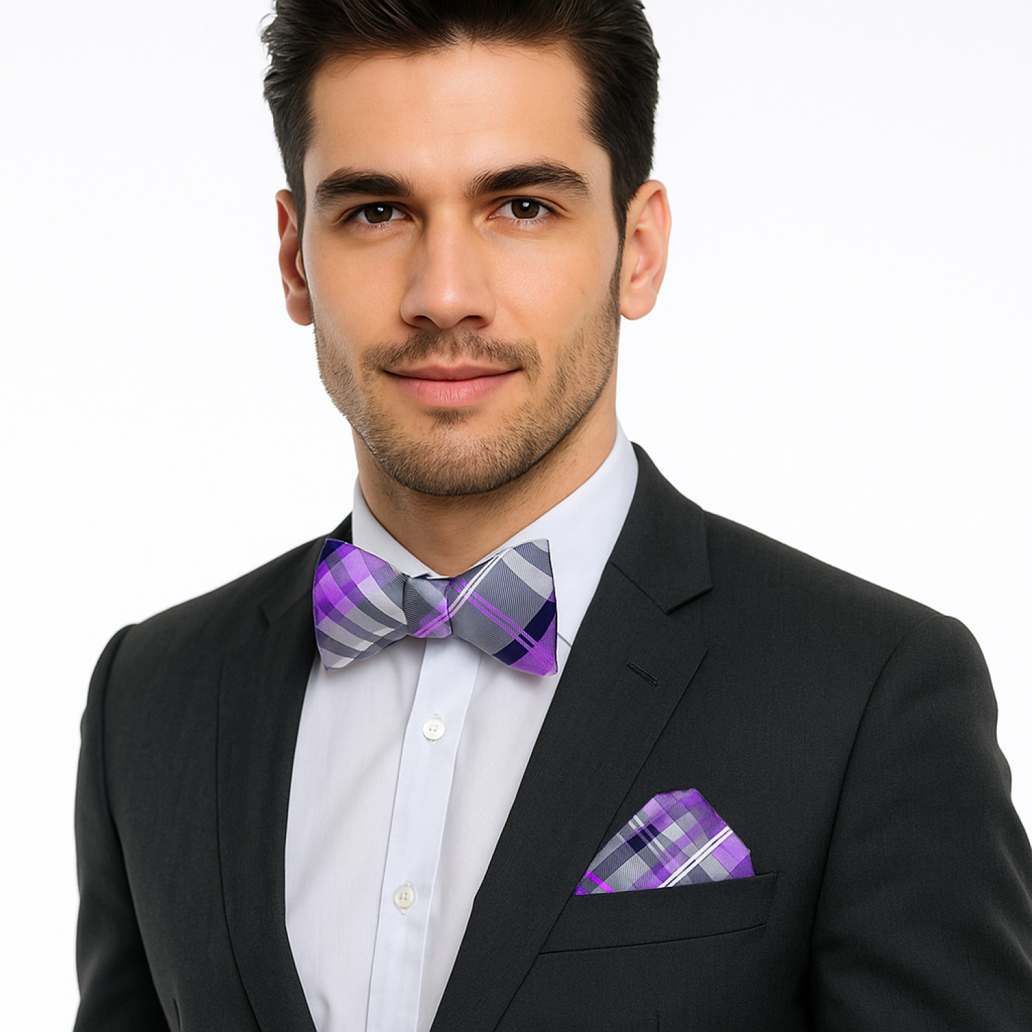 Man wearing a black suit with a purple and gray checkered bow tie and pocket square on a white background