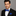 Man wearing a black suit with a blue bow tie and pocket square on a gray background