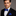 Man wearing a black suit with a white shirt and blue bow tie and pocket square on a gray background