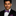 Man wearing a black suit with a colorful red and blue paisley bow tie and pocket square on a gray background
