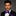 Man wearing a black suit with a purple bow tie against a gray background