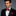 Man wearing a black suit with a Garnet Red Solid Pattern Self Tie Bow Tie, Matching Pocket Square on a gray background