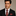 Man wearing a black suit with a red and brown paisley tie and pocket square against a beige background