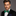 Man wearing a black suit with a green snowflake bow tie and blue red and green Christmas tree patterned pocket square on a gray background