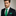 Man wearing a black suit with a green tie and pocket square against a gray background