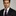 Man wearing a black suit with a purple tie and pocket square on a gray background