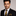 Man wearing a black suit with a gold tie and pocket square against a gray background