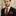 Man wearing a black suit with a red striped tie and pocket square against a neutral background