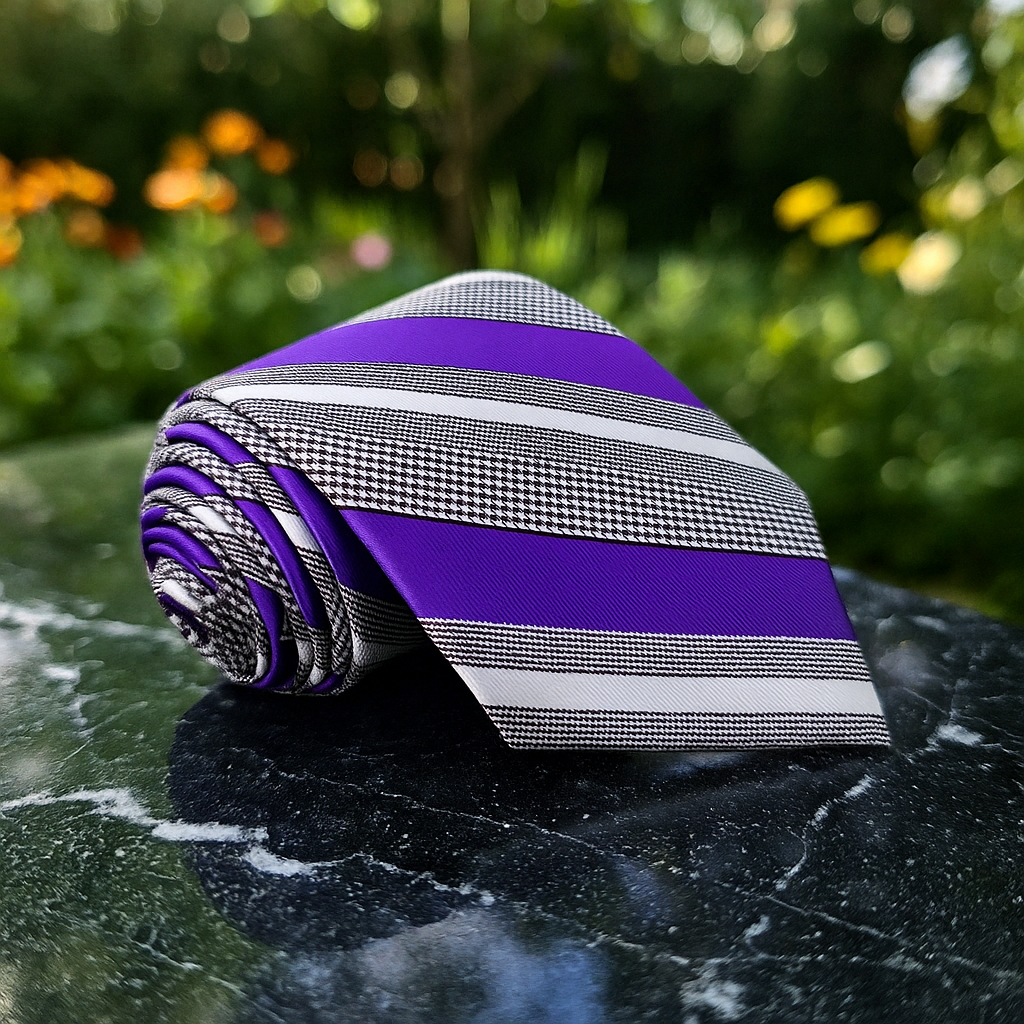 Folded purple and gray striped tie on a dark surface with a blurred natural background