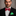 Man wearing a black suit with a red bow tie and green pocket square against a gray background