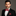 Man wearing a black suit with a red bow tie and matching pocket square on a gray background