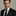 Man wearing a black suit with a green tie and pocket square against a neutral background