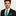 Man wearing a black suit with a green tie and pocket square on a light gray background