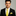 Man wearing a black suit with a yellow tie and pocket square on a gray background