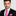Man wearing a black suit with a pink tie and pocket square on a light gray background