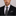 Man wearing a black suit with a patterned tie and pocket square on a gray background
