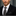 Man wearing a black suit with a patterned tie against a blurred background