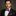 Man wearing a black suit with a colorful bow tie and pocket square on a gray background