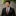 Man wearing a black suit with an orange patterned tie and pocket square against a stone wall.