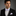 Man wearing a black suit with a white shirt and patterned bow tie and pocket square on a gray background