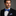 Man wearing a black suit with a blue bow tie and pocket square on a gray background