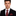 Man wearing a black suit with a red and black checkered tie and pocket square on a white background