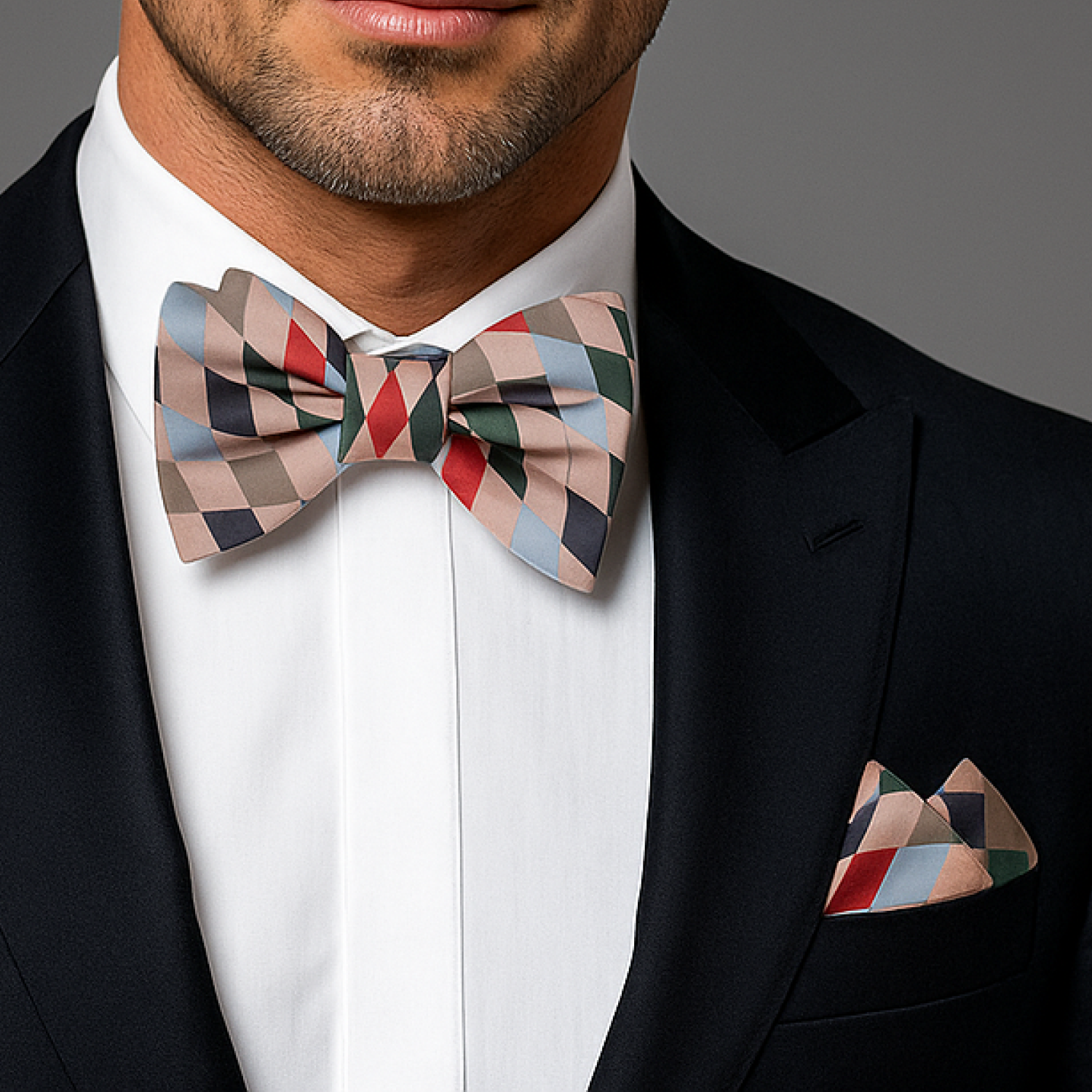 Man wearing a patterned bow tie and matching pocket square against a gray background
