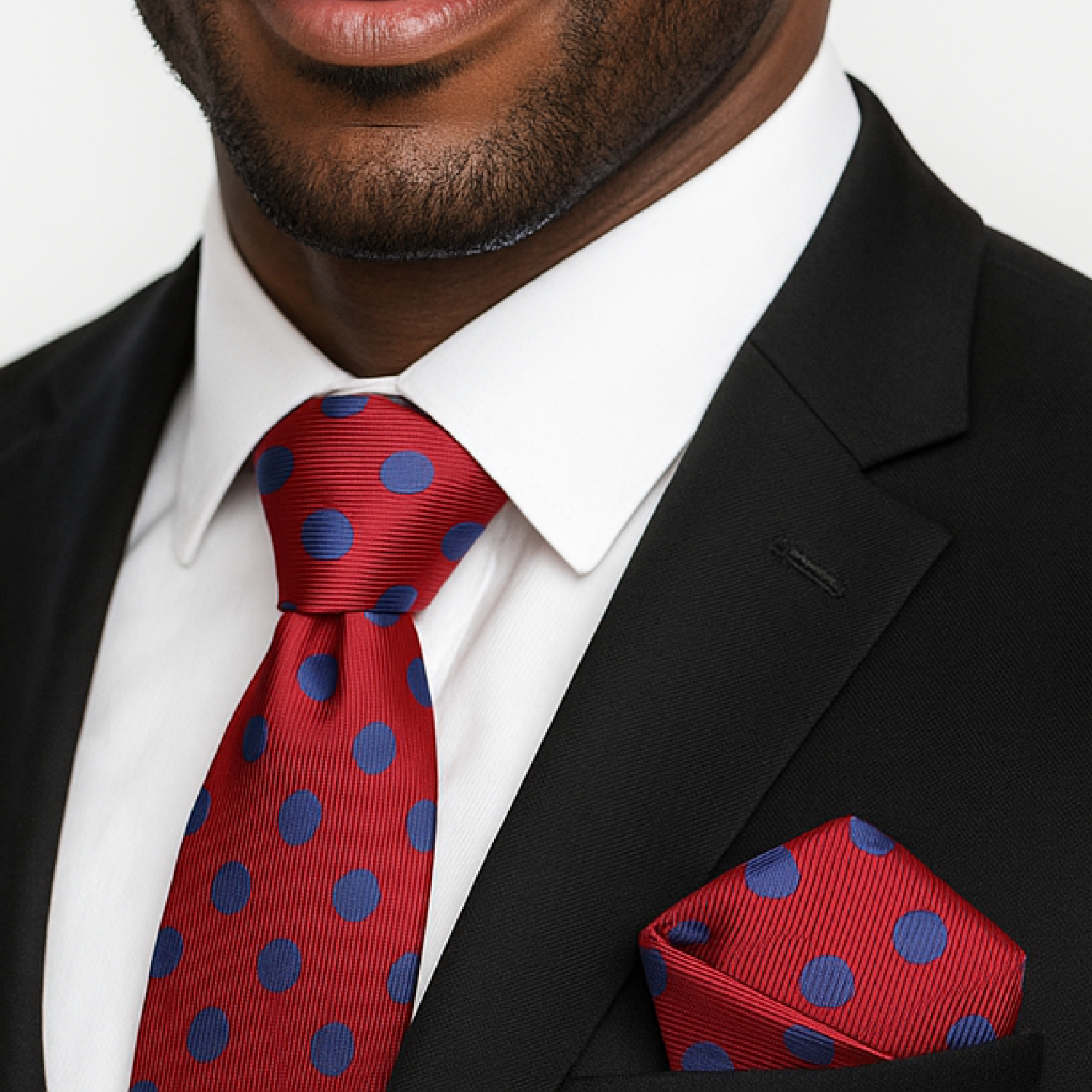 Man wearing a black suit with a red tie and matching pocket square featuring blue polka dots.