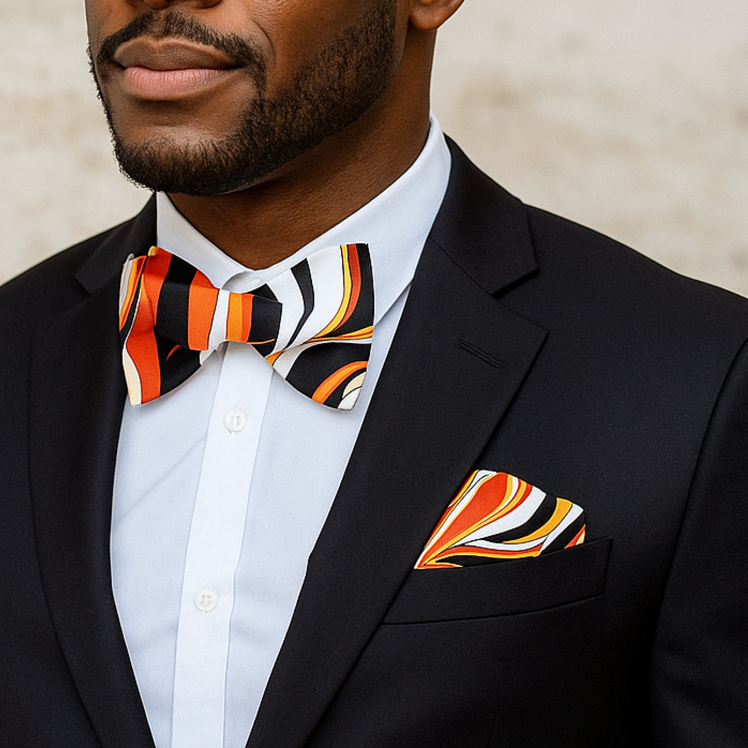 Man wearing a black suit with a colorful striped bow tie and pocket square.